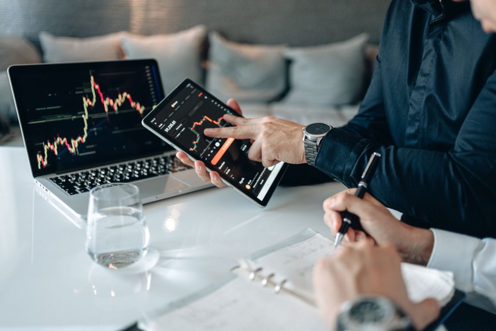 Profissionais analisam dados financeiros em um tablet e um laptop em um ambiente de escritório.